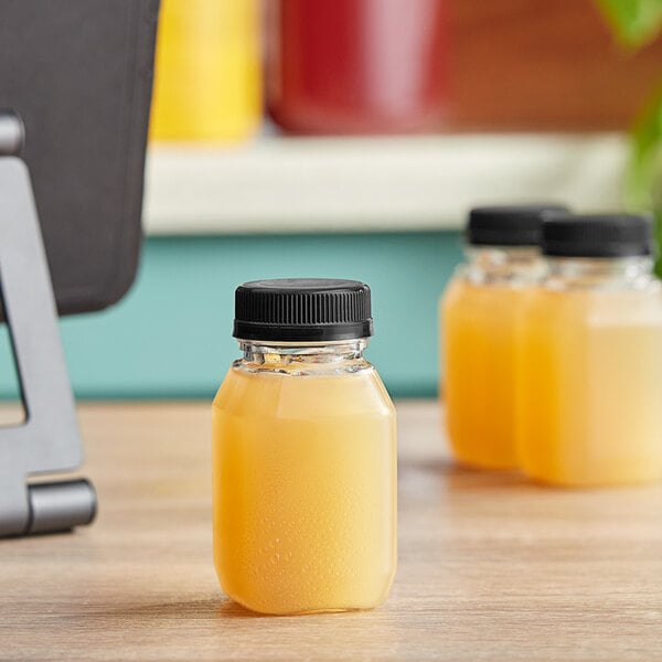 A 4 oz. square clear PET bottle of orange juice with a black lid.