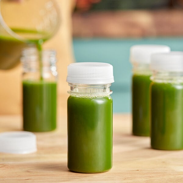 A person pouring green juice into 2.5 oz. round PET clear energy bottles.