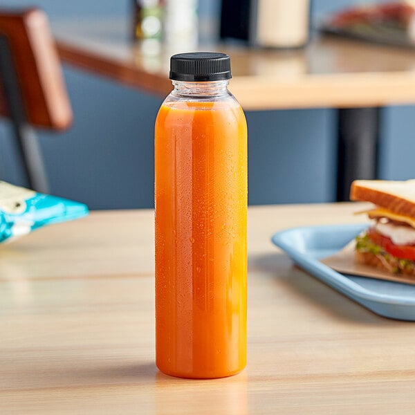 A 16 oz. round PET clear juice bottle of orange juice on a table.