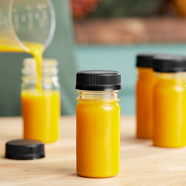 A group of 2.5 oz. yellow PET round bottles with black lids filled with orange liquid.