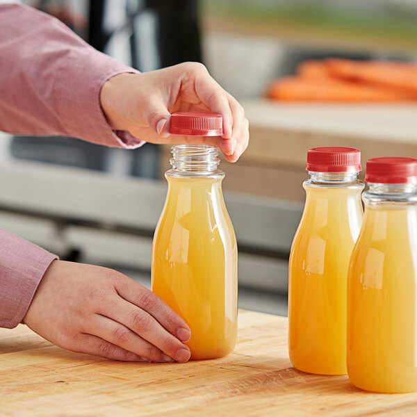 A person pouring orange juice into a 12 oz. round PET clear carafe juice bottle.