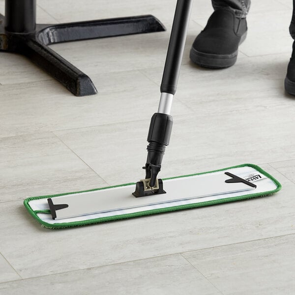 A person using a Lavex green microfiber mop pad on a floor with a mop handle.