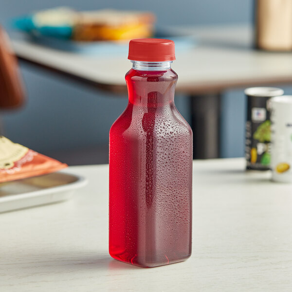 A 16 oz. square clear PET juice bottle with a red lid on a table.