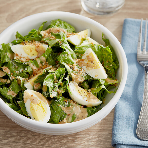 A bowl of salad with hard boiled eggs and bacon next to a bowl of salad with dressing.