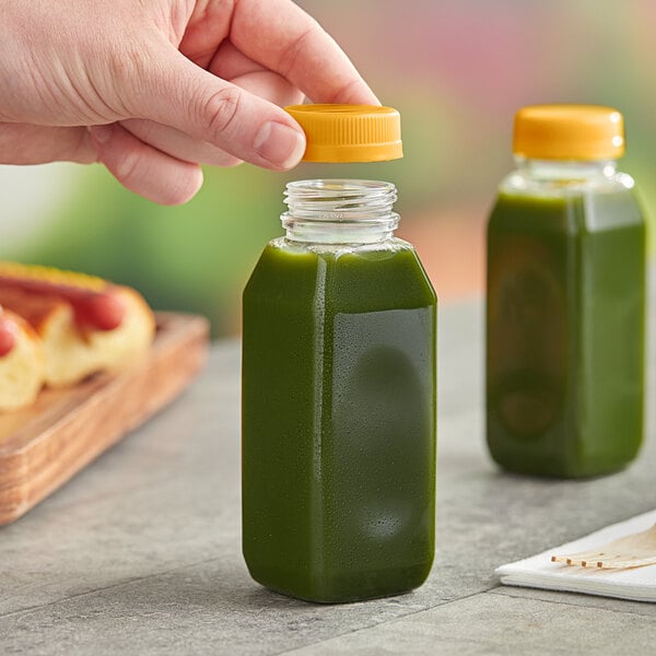 A hand holding a bottle of green liquid with an orange lid.