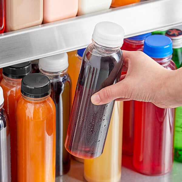 A hand holding a round PET clear juice bottle.