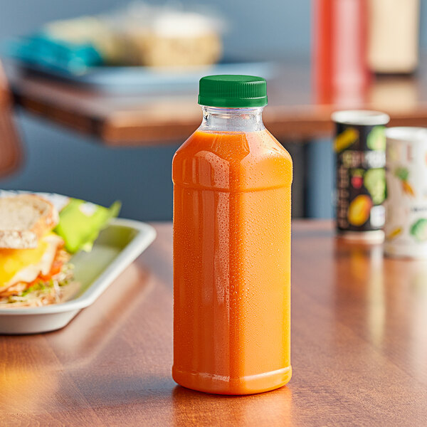 A 14.5 oz. square PET clear juice bottle with a green lid on a table next to a sandwich.