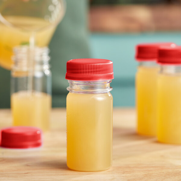 A person pouring yellow liquid into small round PET bottles with red lids.