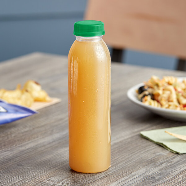 A round clear rPET juice bottle with a green lid on a table next to food.