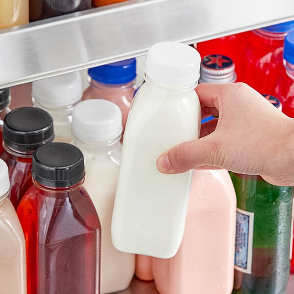 A person holding a 12 oz. Square Milkman clear juice bottle with pink liquid.