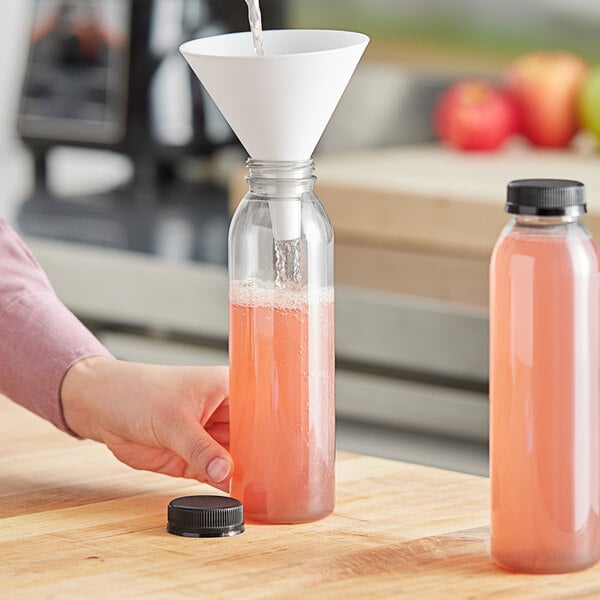 A person pouring pink liquid into a clear round PET juice bottle.