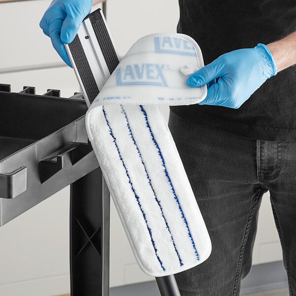 A person wearing blue and white gloves scrubs a stove with a Lavex Microfiber Wet Mop Pad.