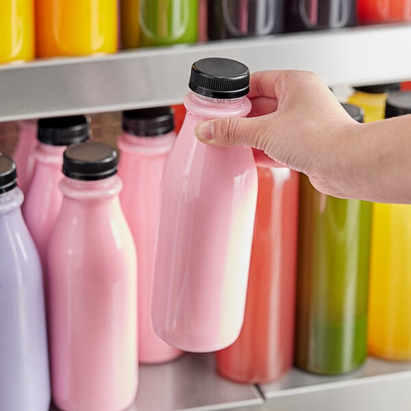 A hand holding a 16 oz. round clear PET juice bottle filled with pink liquid.