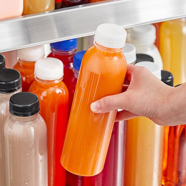 A hand holding a 16 oz. round clear plastic bottle of orange juice.