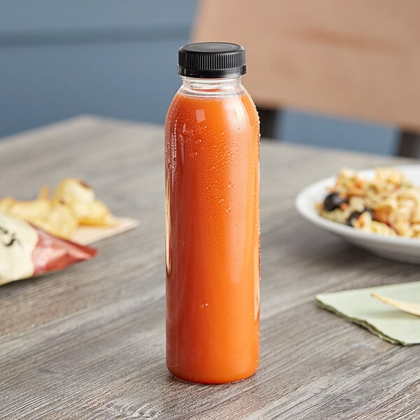 A 12 oz. round rPET clear juice bottle with a black lid on a table next to a plate of food.