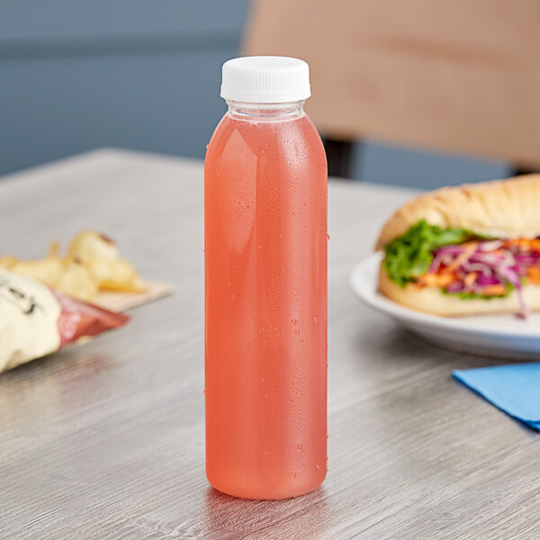 A 12 oz. round clear rPET juice bottle with pink liquid on a table next to a sandwich.