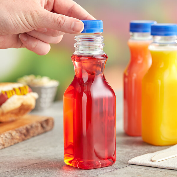 A hand holding a 10 oz. square clear PET juice bottle with blue liquid inside.