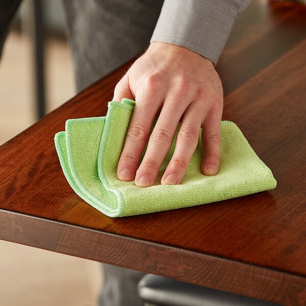 A hand holding a green Lavex microfiber cloth cleaning a table.