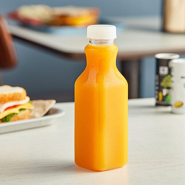 A Square PET clear juice bottle with a clear lid on a table next to a sandwich.