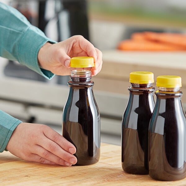 A person pouring liquid from a 12 oz. round PET clear carafe juice bottle into a cup.