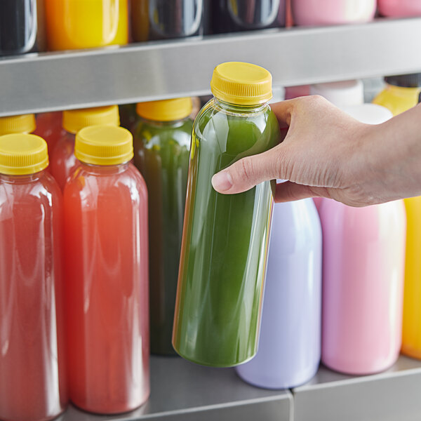 A hand holding a 16 oz. round clear juice bottle with yellow liquid.