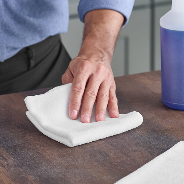 A hand wiping a table with a white Lavex microfiber cloth.