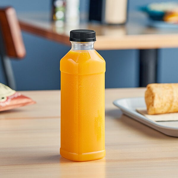 A 16 oz. clear square PET juice bottle with a black lid on a table.