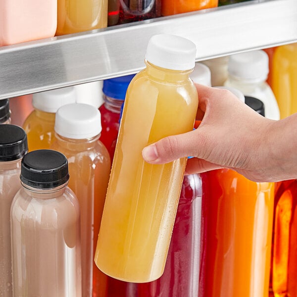 A hand holding a 16 oz. round clear PET juice bottle with white lid.