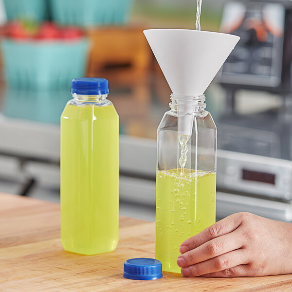 A hand pouring juice into a 12 oz. clear square PET juice bottle with a blue lid.
