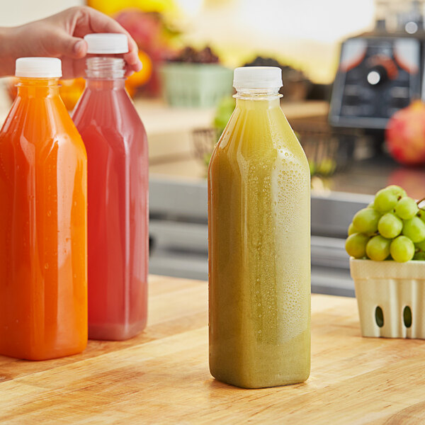 A person holding a 32 oz. clear juice bottle with green liquid and a white lid.