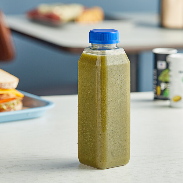 A 16 oz. clear rPET juice bottle filled with green liquid on a table next to a sandwich.
