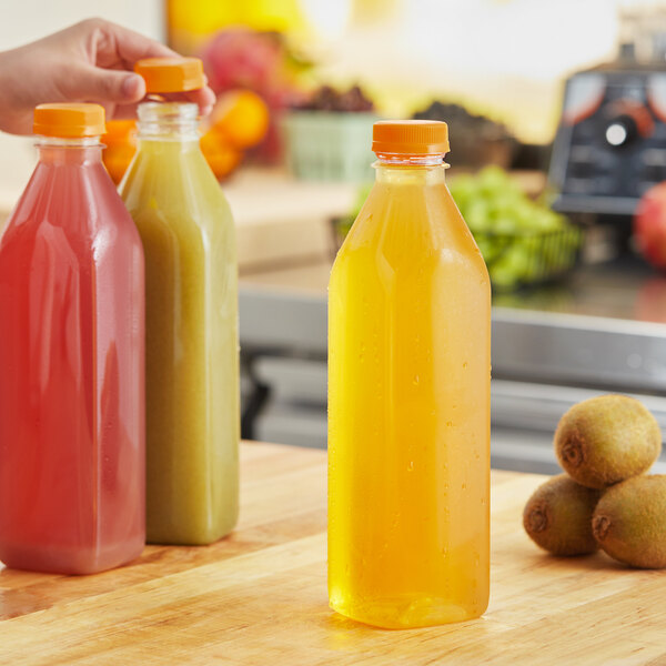 A person's hand holding a tall square clear juice bottle with orange liquid.