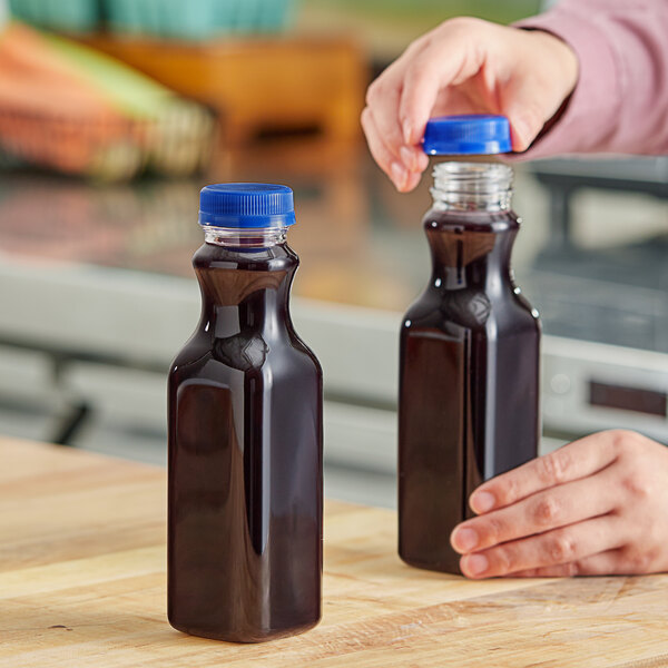 A person pouring juice into a Square PET clear juice bottle with a blue lid on a counter.