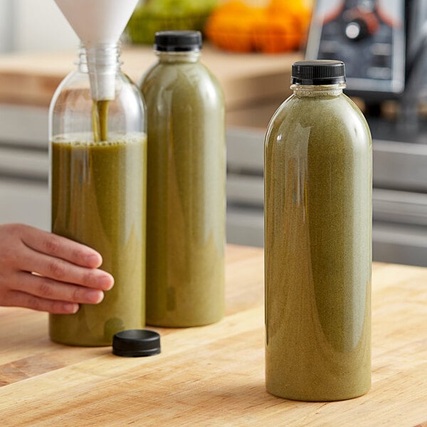 A hand pouring green juice into two 32 oz. round PET clear juice bottles.