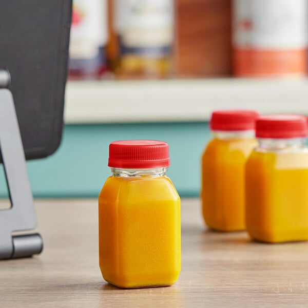 Three 4 oz. square PET bottles of orange juice with red lids on a counter.
