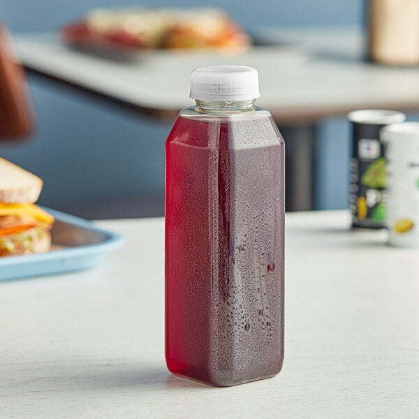 A 16 oz. tall square rPET clear juice bottle filled with red liquid on a table.