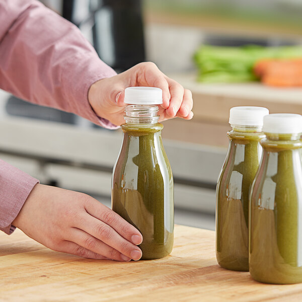 A person pouring green juice into a round clear carafe juice bottle.