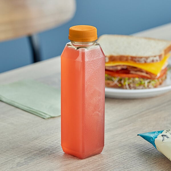 A sandwich next to a 12 oz. clear rPET square juice bottle with orange liquid.