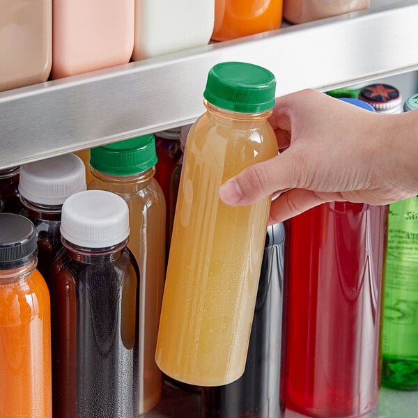 A hand holding a 12 oz. round PET clear juice bottle with dark green liquid.