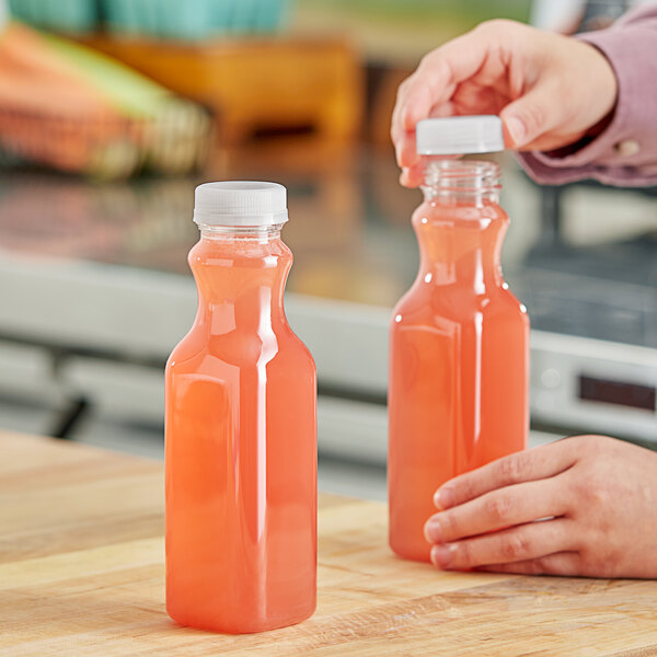 A person pouring orange juice into a 12 oz. square PET clear carafe juice bottle.