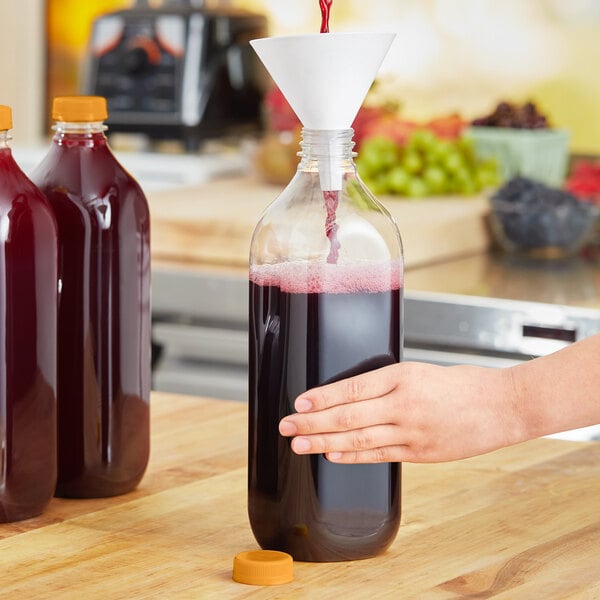 A person pouring juice into a Square PET clear juice bottle with an orange lid.