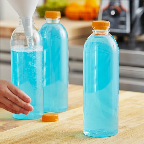 A hand pouring orange liquid into a clear juice bottle on a counter.