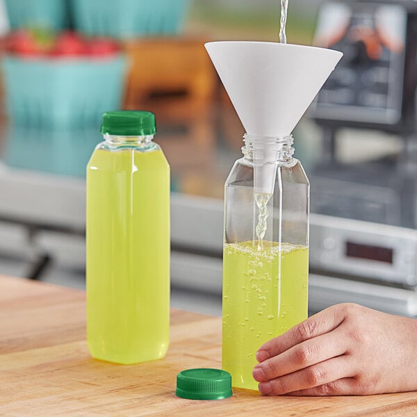 A hand pouring yellow liquid into a 12 oz. clear square PET juice bottle.