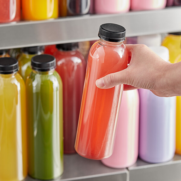 A hand holding a round clear rPET juice bottle filled with yellow liquid.