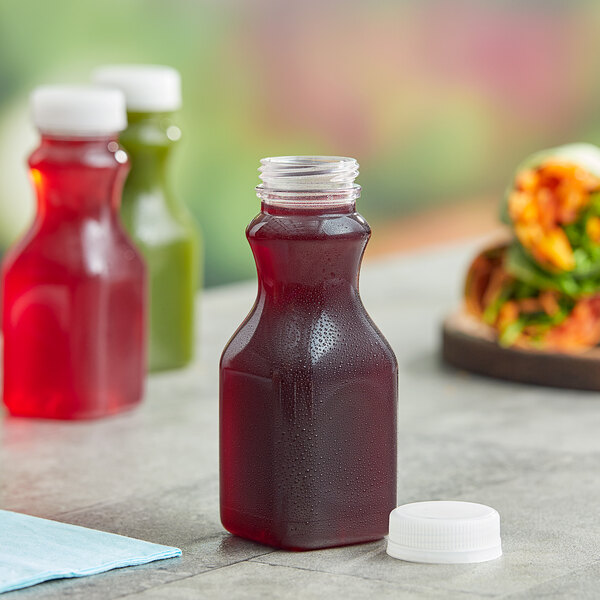 A Square PET clear juice bottle with a clear lid of liquid on a table next to food.