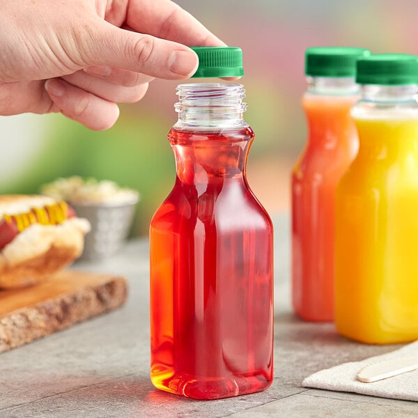 A hand holding a 10 oz. square PET clear carafe juice bottle with green liquid.