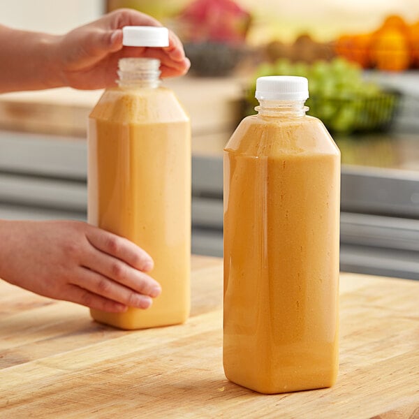 A hand holding a 32 oz. square PET clear juice bottle of yellow liquid.