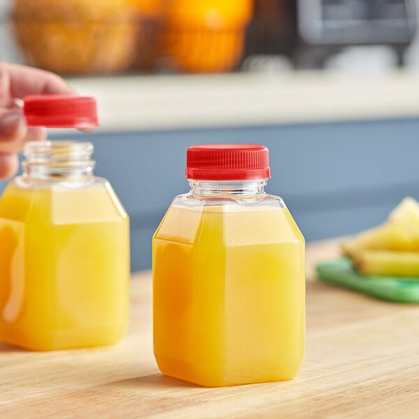 A hand pouring juice from a Square PET clear juice bottle with a red cap.