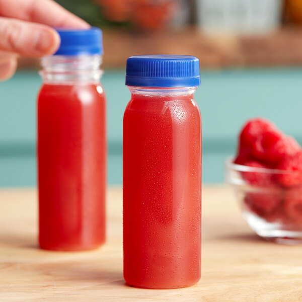 A hand holding a round clear plastic bottle of red raspberry juice.