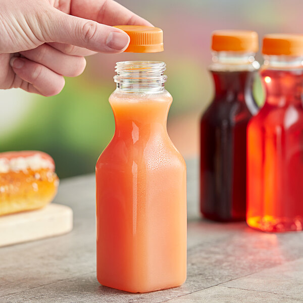 A hand holding a 10 oz. square PET clear carafe juice bottle of orange juice.